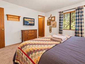 A bedroom with a bed, a dresser, a painting, and a window with curtains. - Grizzly's Getaway (Sugarloaf)
