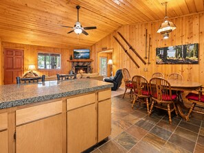A wooden interior with a stone fireplace, a dining area with wooden chairs, a kitchen with granite countertops, and a ceiling fan. - Grizzly's Getaway (Sugarloaf)