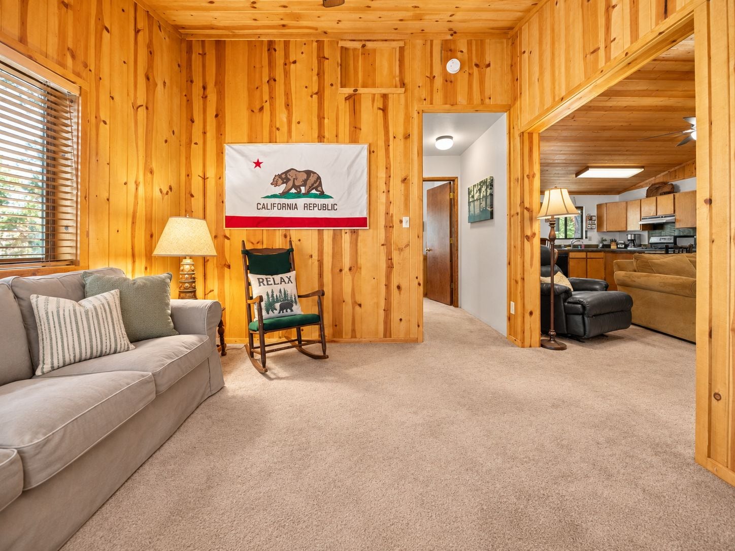 Une pièce chaleureuse avec un décor intérieur en bois, un drapeau accroché au mur, un fauteuil à bascule, un canapé et un coin cuisine.