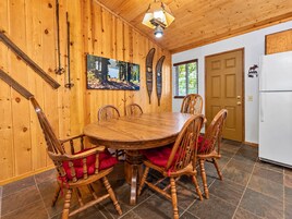 A wooden dining room with a round table and chairs, a painting on the wall, and a door with a window.