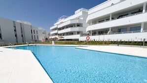 A modern building with a swimming pool, balconies, and a clear sky.