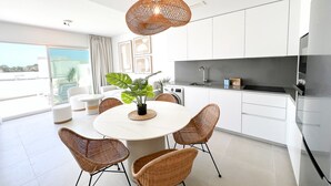 A modern kitchen with white cabinets, a round dining table with wicker chairs, and a hanging light fixture.