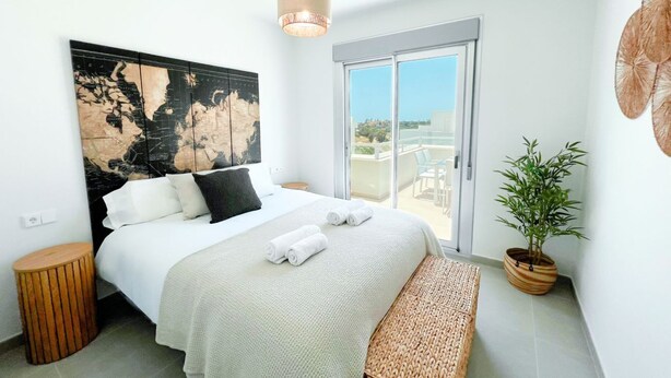 A bedroom with a bed, a large abstract painting, a potted plant, and a view through a glass door.