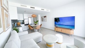 A modern living room with a sofa, a round coffee table, and a flat-screen TV displaying a beach scene.