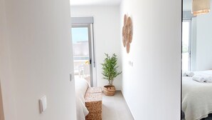 A narrow hallway with a bed, a potted plant, a woven bench, and a wall-mounted decoration.