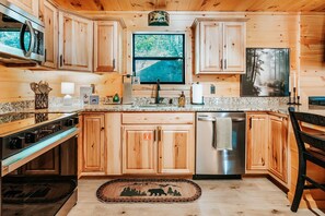 Une cuisine rustique, située dans une cabane en bois, équipée d’une cuisinière, d’un four à micro-ondes, d’un évier et d’un lave-vaisselle en acier inoxydable.