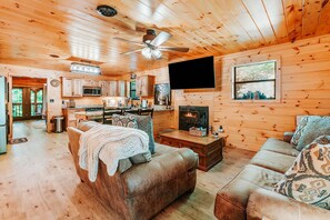 Un intérieur de chalet chaleureux comprenant un salon, une cuisine et une cheminée.