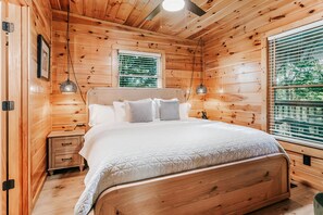 Une chambre dans une cabane en bois, avec un lit, des tables de chevet et une fenêtre avec des stores.
