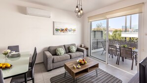 A modern living room with a grey sofa, a glass dining table, and a balcony with outdoor furniture. - 2 bedroom apartment in Kapparis AK14 (Kapparis)