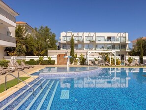 Ein modernes Hotel mit Schwimmbad, Liegestühlen und blauem Himmel.