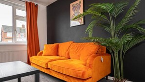 Une pièce avec un mur noir, un canapé orange, une fenêtre avec des rideaux orange, un tableau et une grande plante verte.