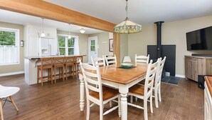 A spacious kitchen with wooden flooring, white cabinetry, and a dining area with a wooden table and white chairs.