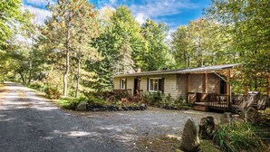 A cabin with a porch, surrounded by trees and a gravel driveway.