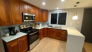 A modern kitchen with wooden cabinets, stainless steel appliances, a double sink, and a window with blinds.