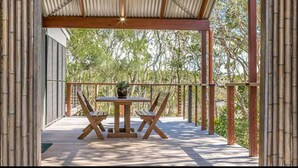 An outdoor patio with a table and chairs, surrounded by bamboo pillars and a corrugated metal roof.