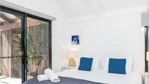 A modern bedroom with a large bed, a small bedside table, and a window with a view of the outdoors.