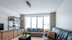 Una sala de estar moderna con un sofá de cuero, un mueble de madera, un televisor y una estantería.