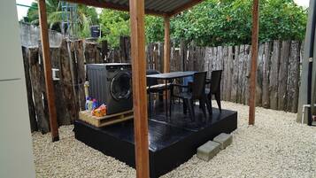 A covered outdoor area with a washing machine, a table, and chairs.