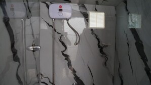 Ein Badezimmer mit Marmorwand, Duschbrause, Wandarmatur und Fenster mit Jalousien.