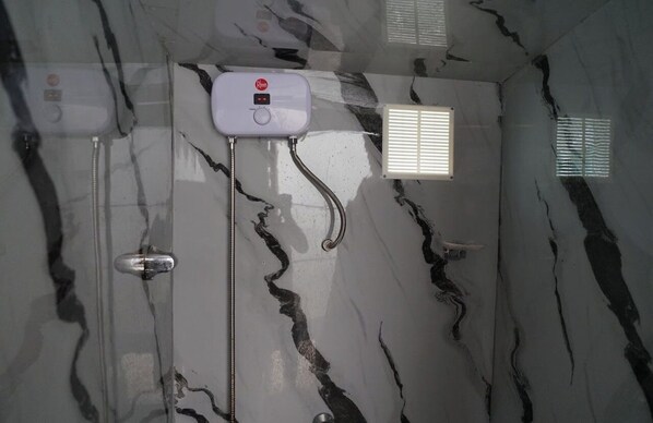 Un baño con pared de mármol, cabezal de ducha de mano, grifo empotrado y una ventana con persianas.