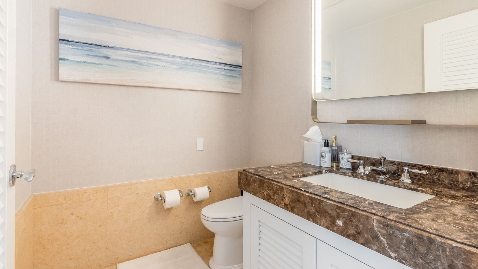 A bathroom with a marble countertop, a toilet, and a painting on the wall.