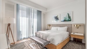 Een moderne hotelkamer met een groot bed, een bankje, een bureau en een schilderij aan de muur.