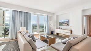 A modern living room with a sofa set, a coffee table, a TV, and a balcony with a city view. - Gorgeous Private Beachfront 2br (Fort Lauderdale)