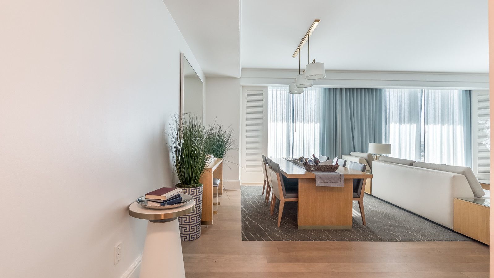 A modern living room with a dining area, a large window with curtains, and a potted plant.