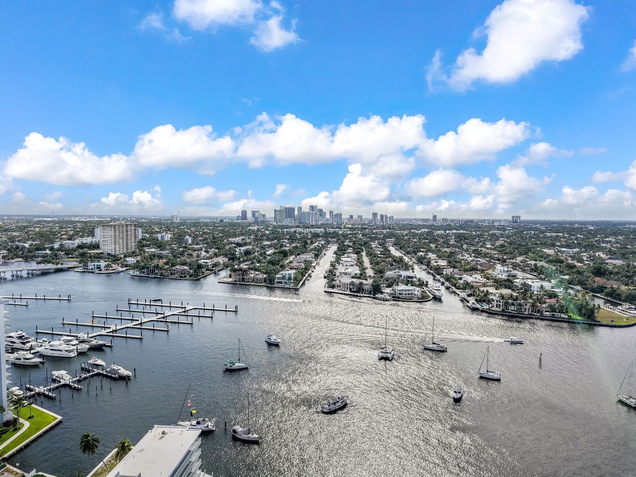 A marina with multiple boats docked, a city skyline in the background, and a clear sky.