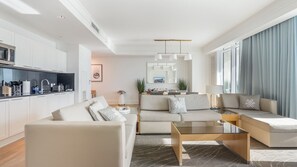 A modern living room with a sofa, coffee table, and kitchen area with white cabinets and appliances. - Gorgeous Private Beachfront 2br (Fort Lauderdale)
