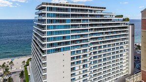 Een meerlaags hotel met balkons, uitzicht op zee en een strand op de achtergrond.