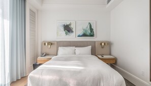 A hotel room with a large bed, two bedside tables with lamps, a window with curtains, and two abstract paintings on the wall. - Gorgeous Private Beachfront 2br (Fort Lauderdale)