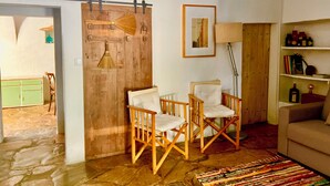 Un salon chaleureux avec une porte en bois, une petite table entourée de chaises, un canapé et une bibliothèque.