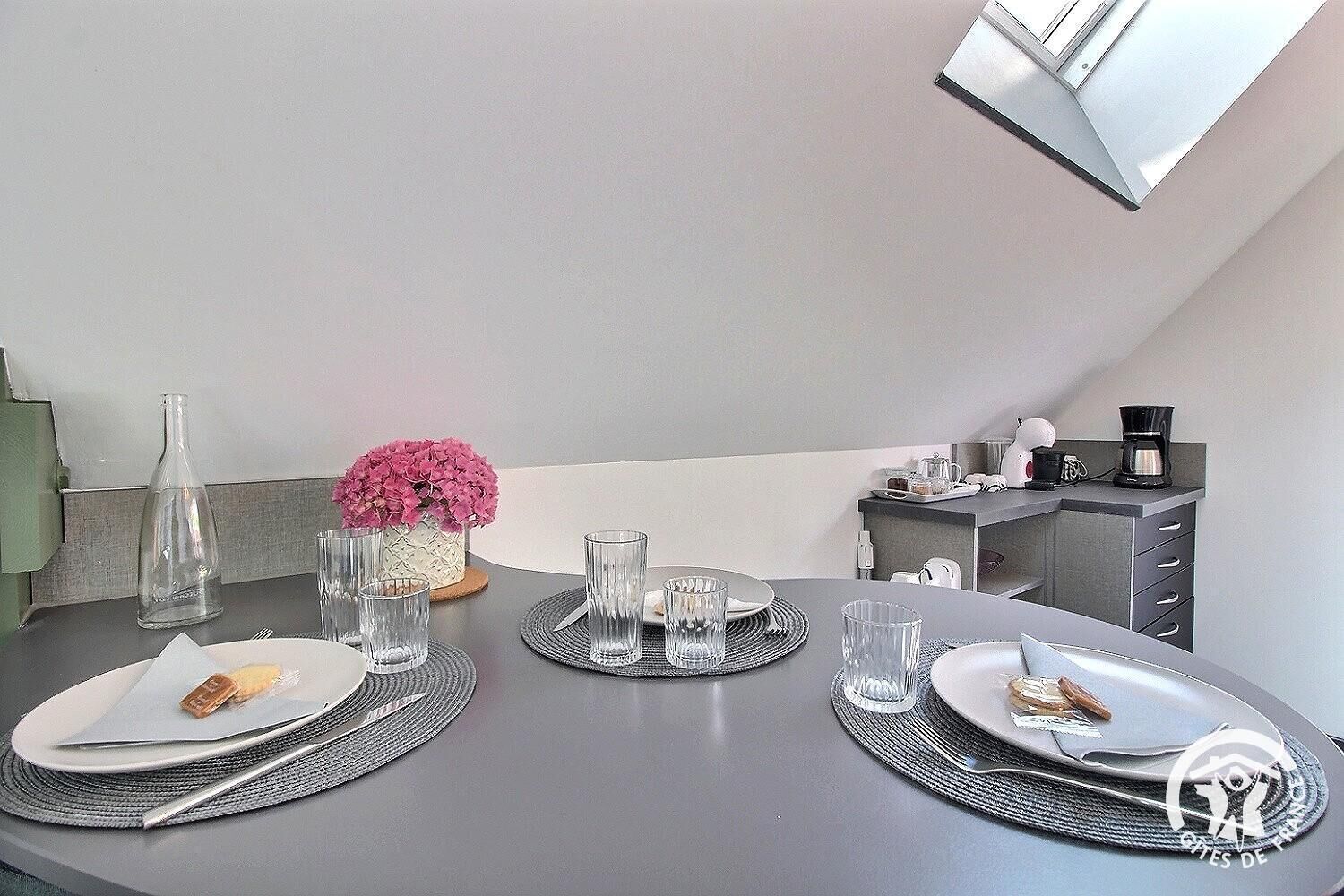 A dining table set with plates, cutlery, glasses, and a vase of pink flowers.