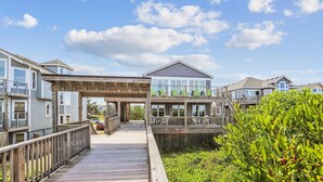 A waterfront residential area with multiple houses connected by a wooden boardwalk. - Beachfront Duck retreat with 4 king bedrooms, 3 baths, and private beach walkway. (Duck)