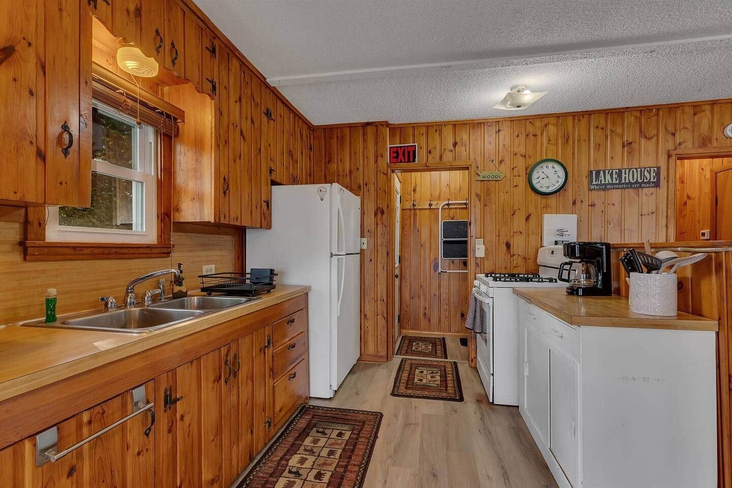A wooden cabin-style kitchen with a sink, stove, refrigerator, and a clock on the wall.