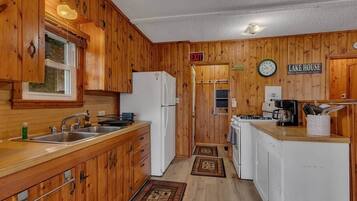 A wooden cabin-style kitchen with a sink, stove, refrigerator, and a clock on the wall.