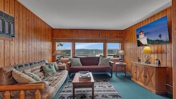 Une pièce confortable, aménagée comme un chalet, avec un intérieur en bois, une grande fenêtre donnant sur l’extérieur, un canapé, une table basse et un meuble contenant des objets décoratifs.