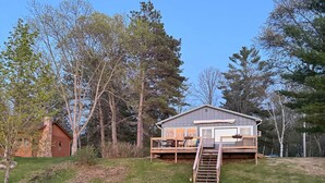 A house with a deck, a fire pit, and two Adirondack chairs in the yard. - The Cozy Cub (Crosslake)