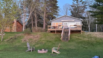 Une maison avec une terrasse, un foyer extérieur et deux chaises Adirondack dans le jardin.