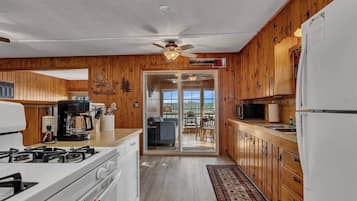 A kitchen with wooden cabinets, a stove, a microwave, and a refrigerator. There is a ceiling fan and a view of a balcony with outdoor furniture.