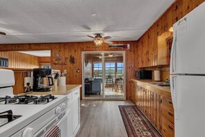 A kitchen with wooden cabinets, a stove, a microwave, and a refrigerator. There is a ceiling fan and a view of a balcony with outdoor furniture. - The Cozy Cub (Crosslake)