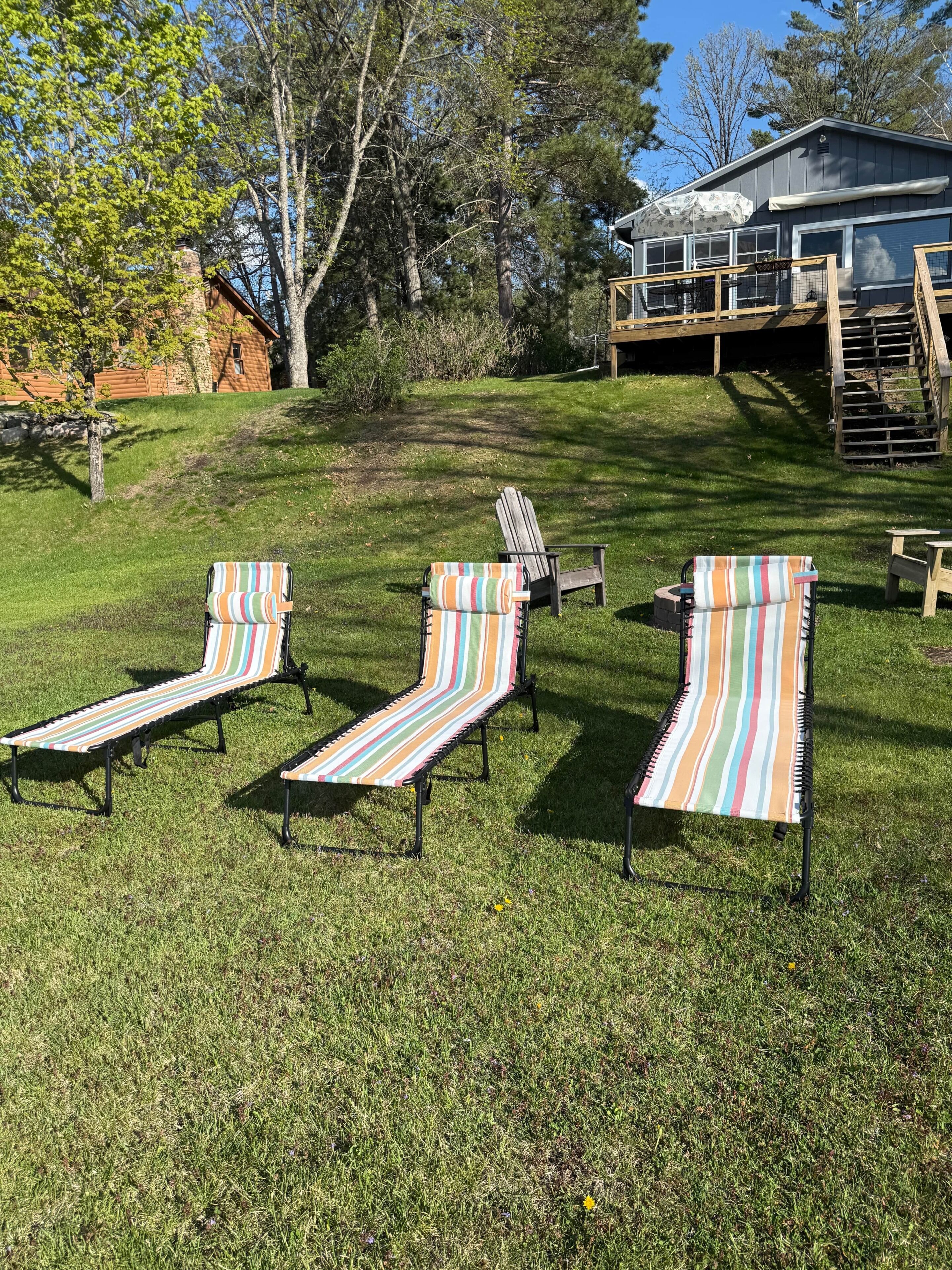 A grassy backyard with three striped lounge chairs and a wooden deck with a staircase.