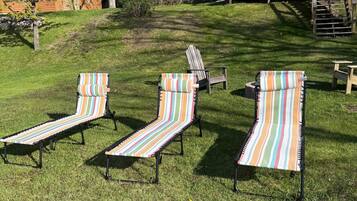 A grassy backyard with three striped lounge chairs and a wooden deck with a staircase.