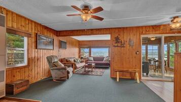 Un intérieur en bois avec un ventilateur de plafond, un ensemble de canapés et une vue à travers une porte vitrée.