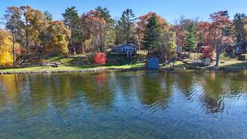 A lakeside property with a dock, a small cabin, and a house with a deck.
