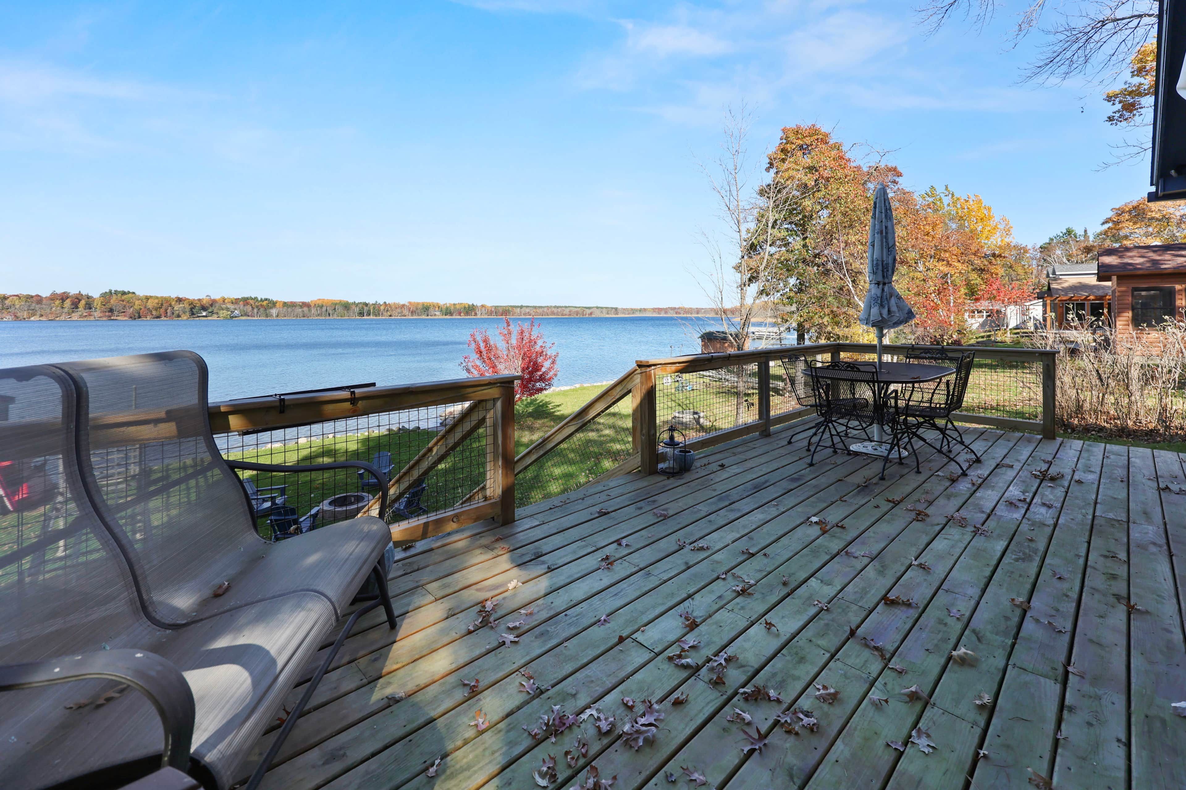 A wooden deck with a view of a lake, a table with chairs, and a covered seating area.