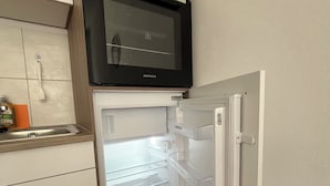 A compact kitchen with a built-in microwave above the refrigerator, a small sink, and a wooden countertop. - Fichtelzimmer - central and modern vacation apartment in the heart of Wunsiedel (Wunsiedel)