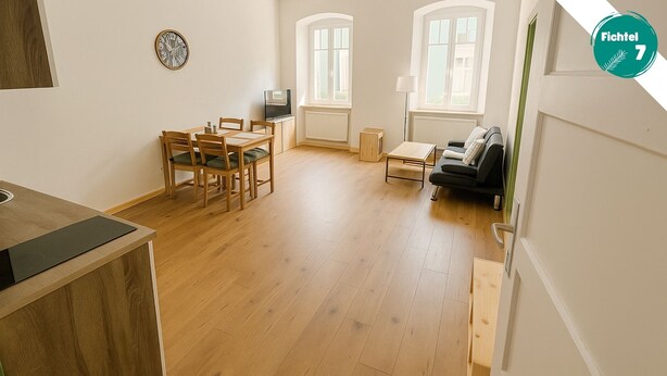 A spacious living area with a wooden floor, a dining table with chairs, a sofa, and a TV. - Fichtelzimmer - central and modern vacation apartment in the heart of Wunsiedel (Wunsiedel)
