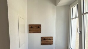 A small, narrow bathroom with white walls, a wooden bench, a window, and two wooden wall-mounted hooks. - Fichtelzimmer - central and modern vacation apartment in the heart of Wunsiedel (Wunsiedel)
